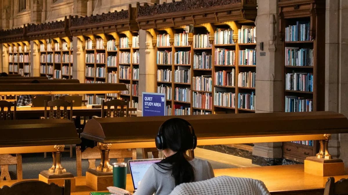 Student with headphones studying on a laptop at a long desk in a quiet college library