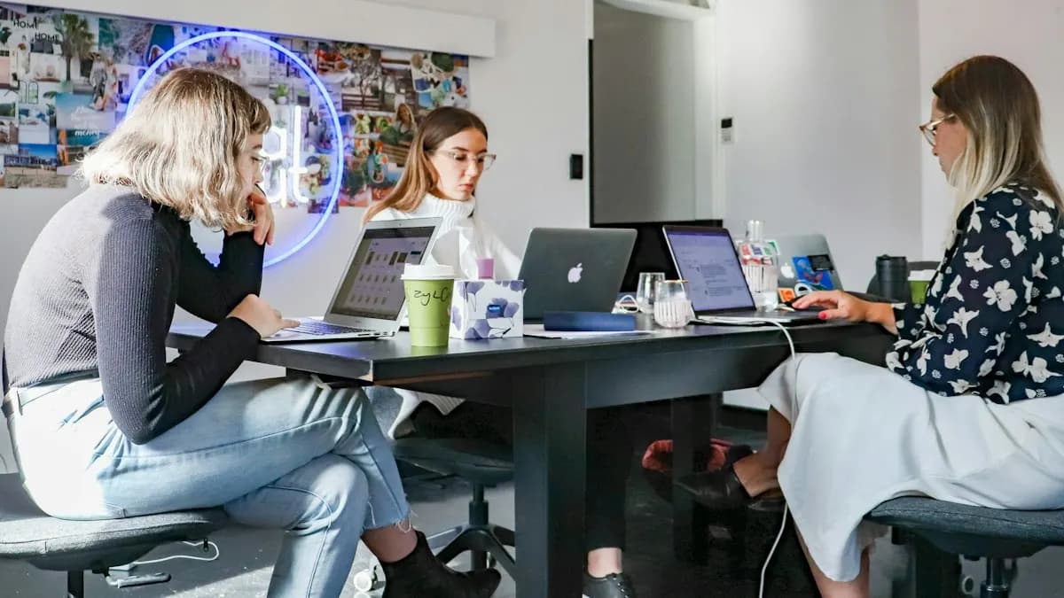 Three young marketers working on laptops around a table in a bright office