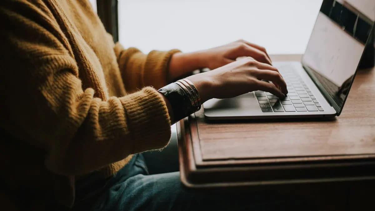 Learner typing on a laptop at a wooden desk during an online digital marketing class