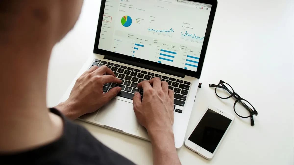 Person typing on a laptop showing a marketing dashboard with charts, next to a phone and glasses