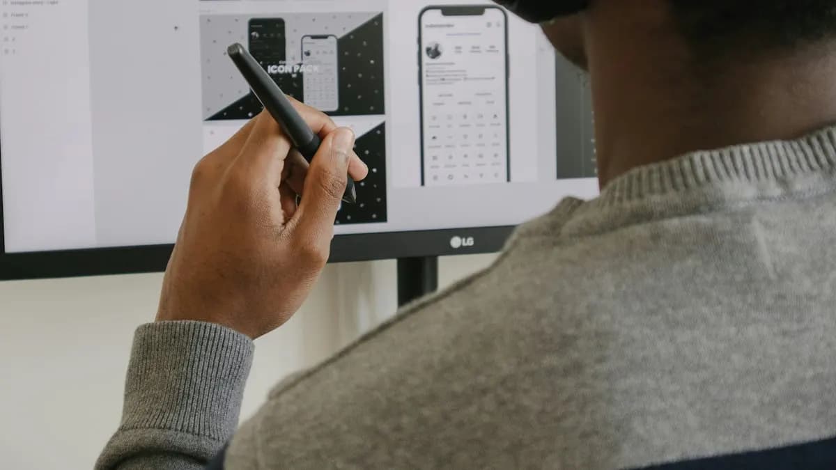 Designer holding a stylus at a monitor showing a mobile app layout he is designing