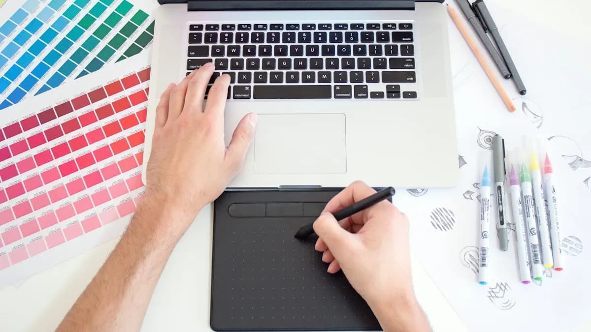 Graphic designer using a pen tablet and laptop beside colour swatches and markers