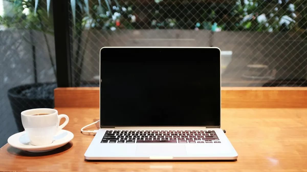 Open laptop and a cup of coffee on a wooden table near a window