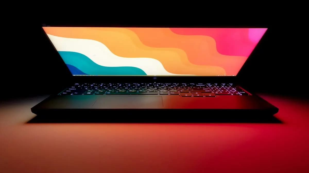 Laptop on a dark desk showing colourful flowing shapes like a motion graphics frame