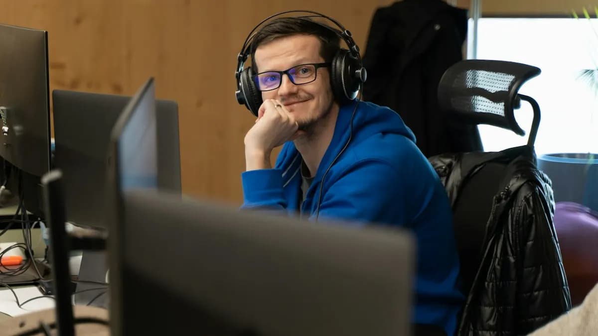 Smiling young man wearing headphones at a video editing desk with two monitors