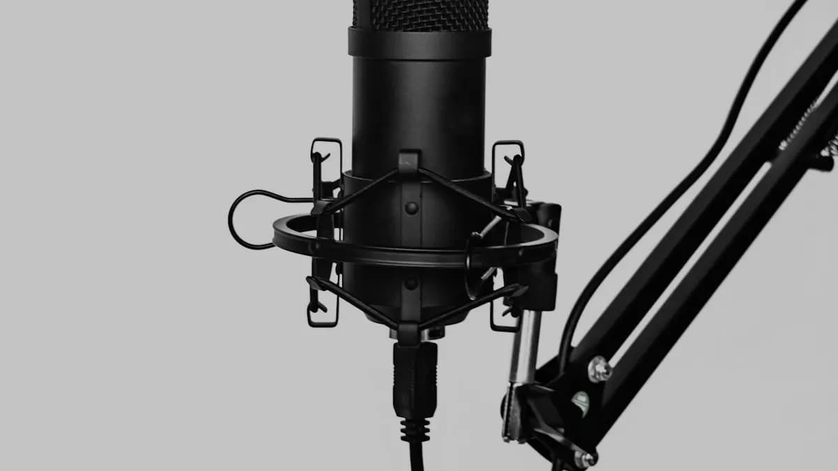 Black condenser microphone in a shock mount on a boom arm against a plain grey wall