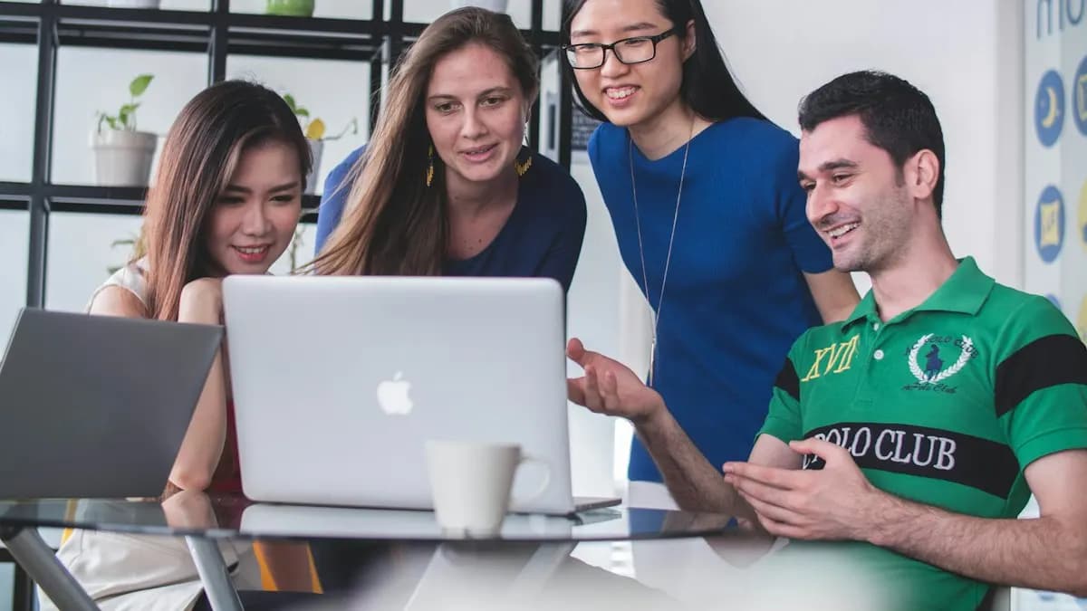 Four young marketers smiling around a laptop while planning a digital marketing campaign