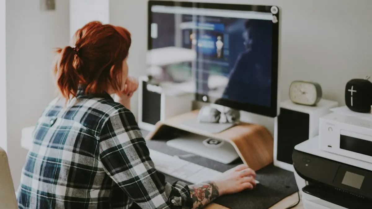 Graphic designer working at a desk with a large monitor in a bright home studio