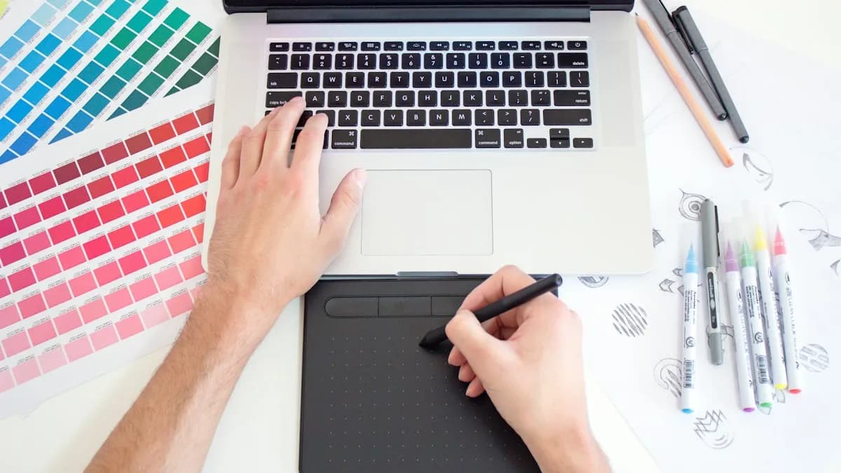Graphic designer working on a laptop with a drawing tablet, colour swatches and sketch pens on the desk