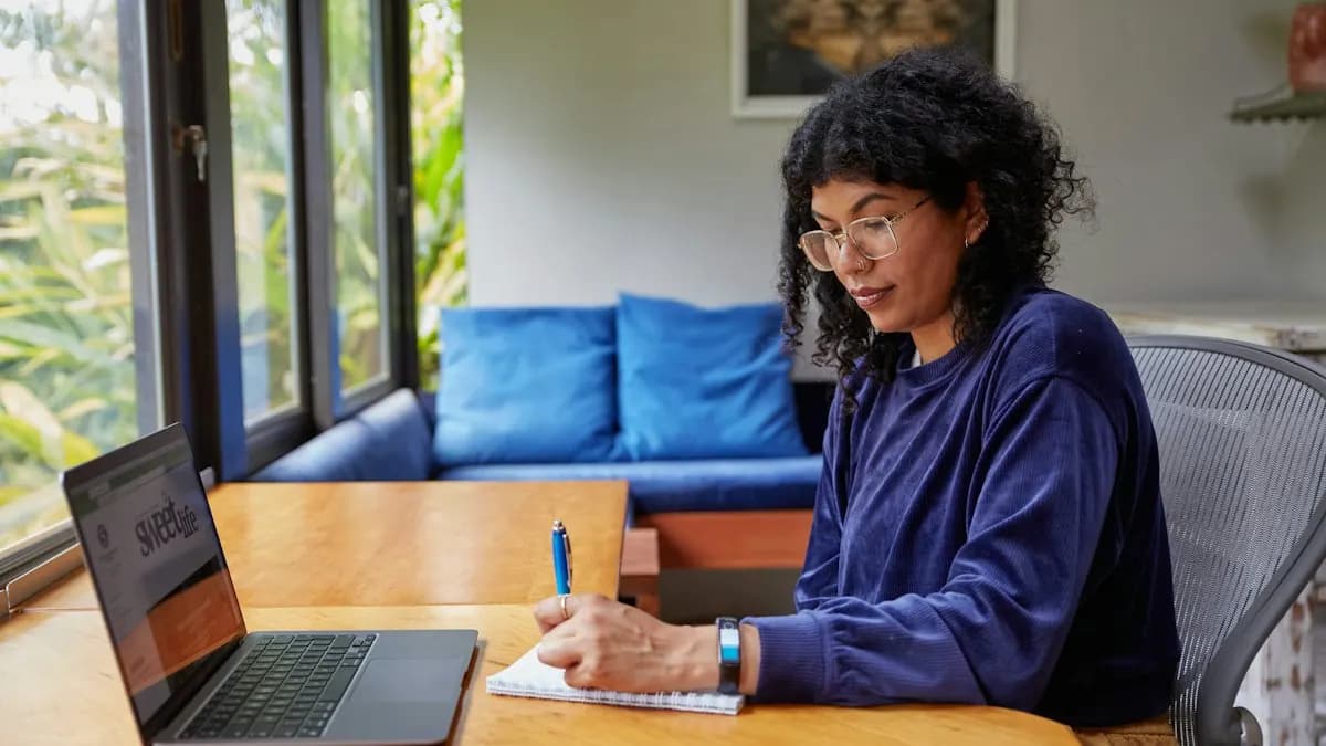Woman writing notes beside her laptop at home while learning graphic design