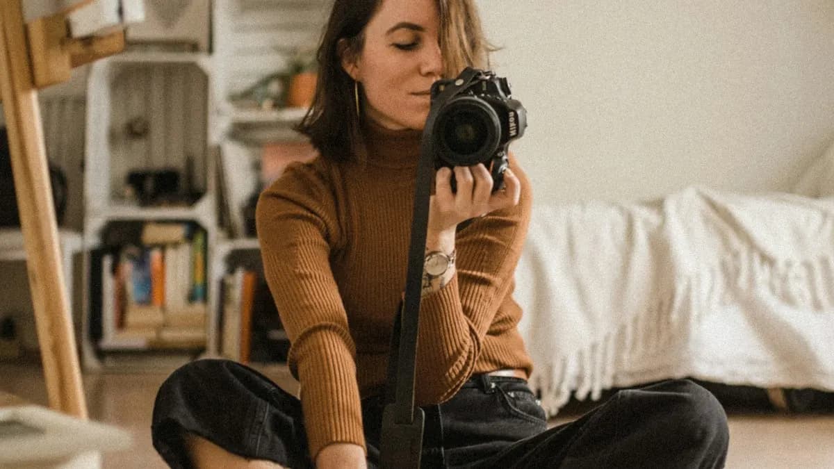 Young photographer sitting on the floor at home holding a camera on a monopod
