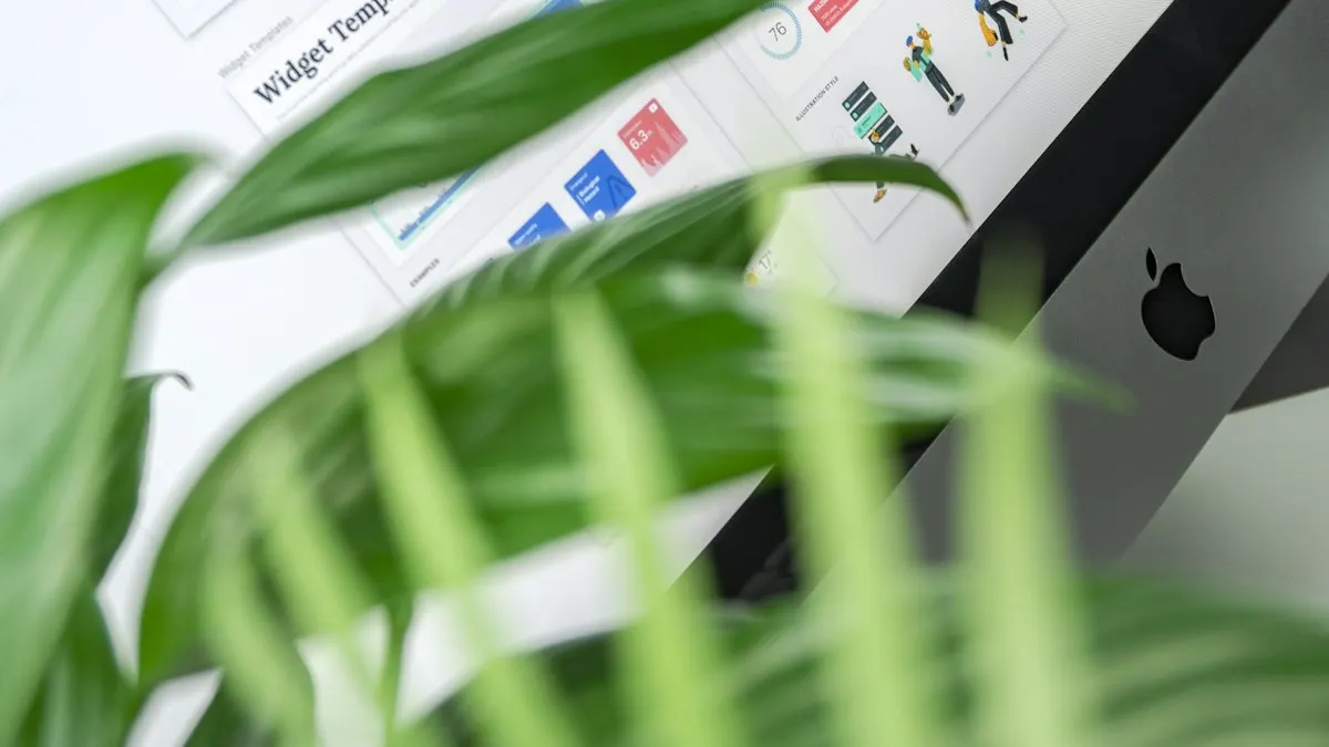 Desktop computer with a design layout on screen seen behind green plant leaves