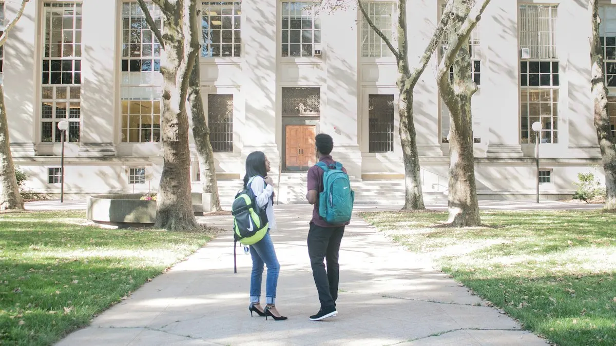 Two college students with backpacks standing on a tree-lined campus path, choosing arts courses after 12th
