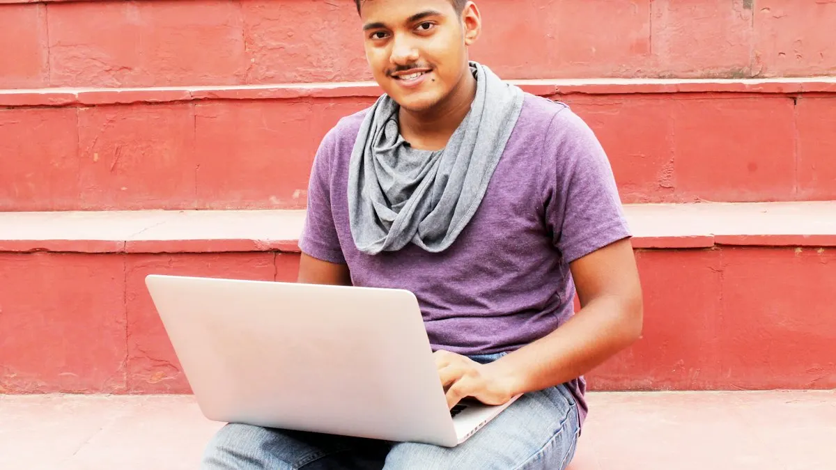 Smiling young man sitting on red steps with a laptop on his lap after class