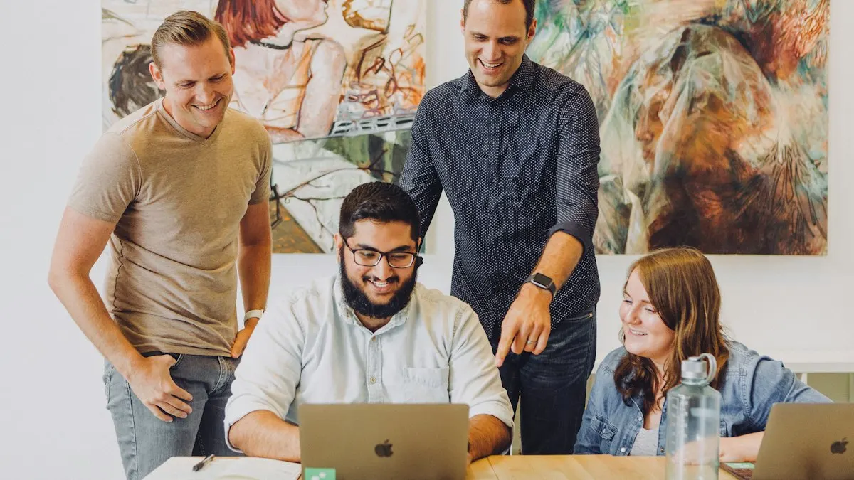 Four young team members smiling while reviewing work on a laptop together