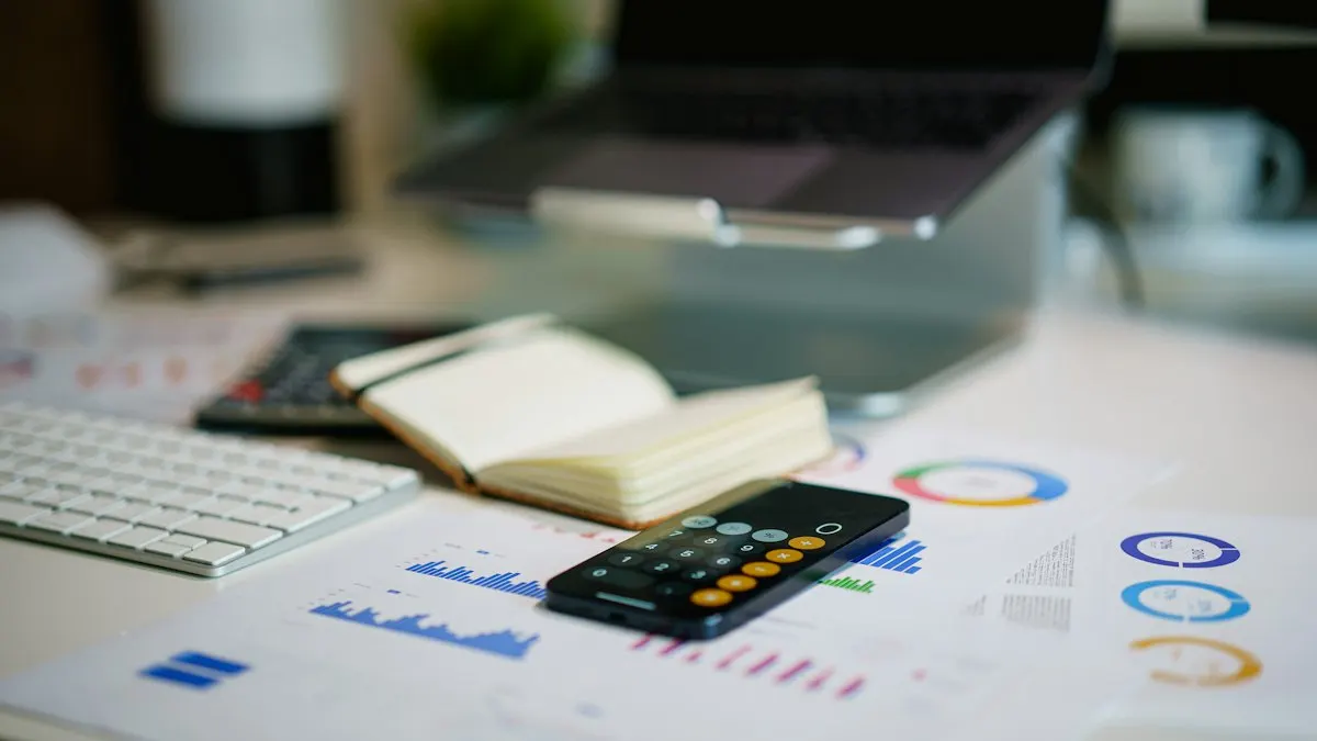 Desk with printed financial charts, a calculator and a laptop used for report and infographic design