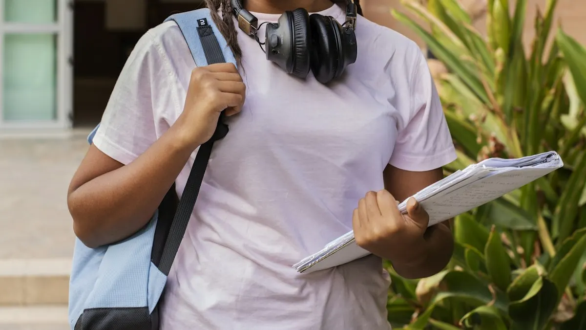 College student with a backpack and headphones holding a notebook outside on campus