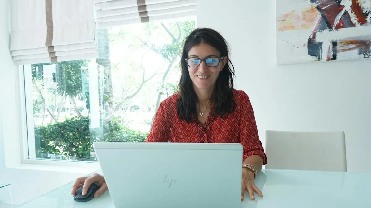 Woman smiling at her laptop while practising graphic design at a bright table at home