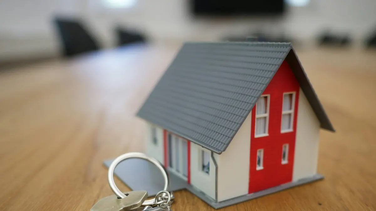 Small model house with a grey roof and a key ring on a wooden table