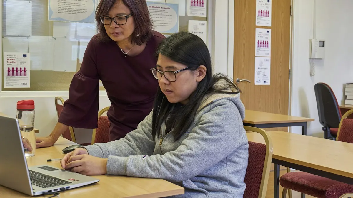 Trainer sitting beside a student and pointing at her laptop screen during a design lesson