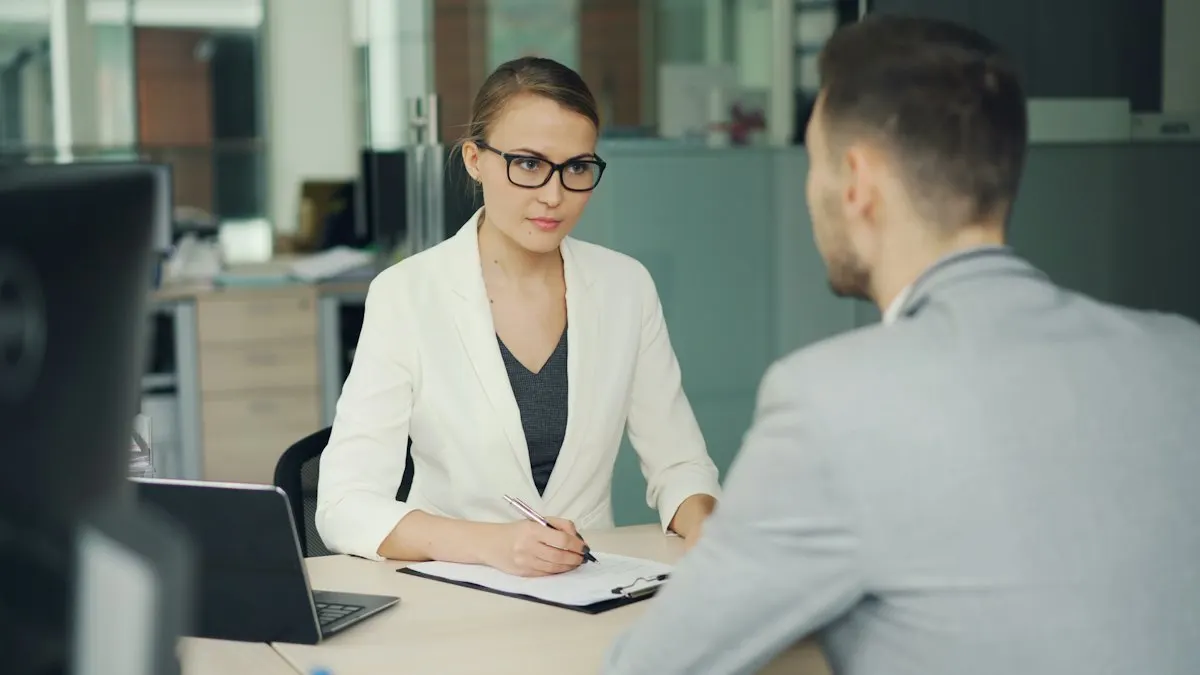 Young woman in a white blazer interviewing a candidate across an office desk with a laptop