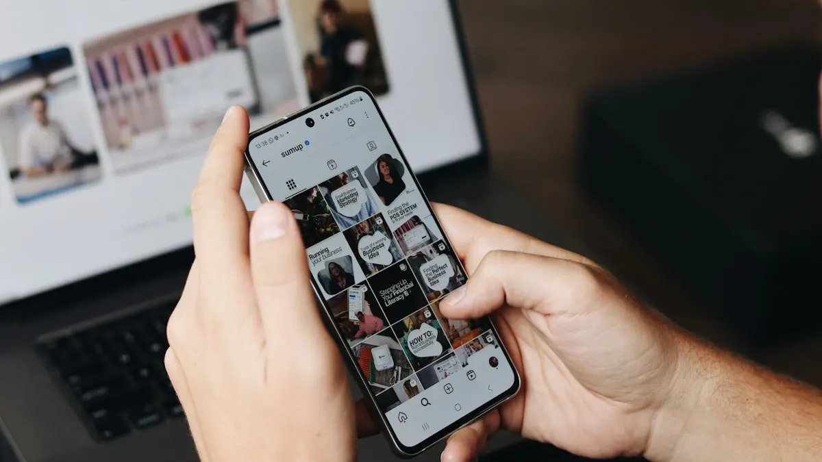 Person checking a social media feed on a phone in front of a laptop with design work