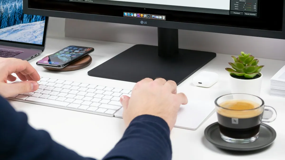 Hands on a white keyboard at a clean design desk with a large monitor and coffee