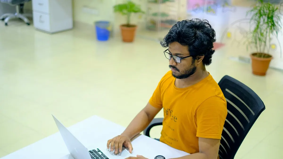 Young man in a yellow t-shirt working on a laptop at an office desk