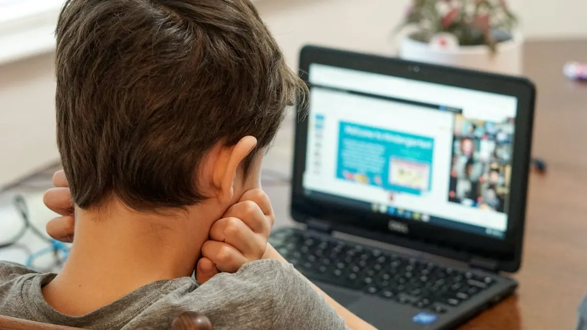 Boy in a grey shirt attending a live online class on a black laptop at home